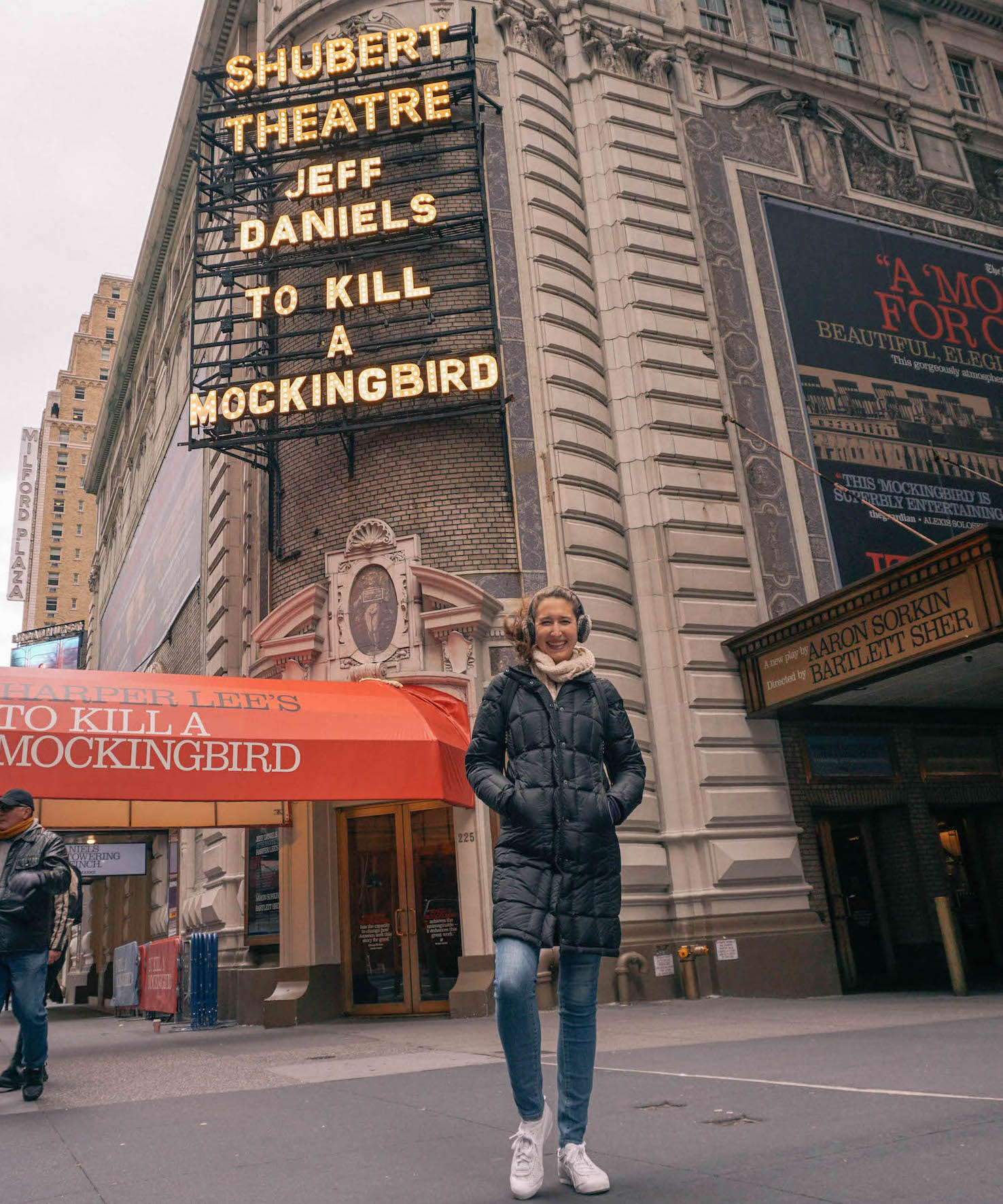 Woman smiling down at camera in front of Broadway show sign. 