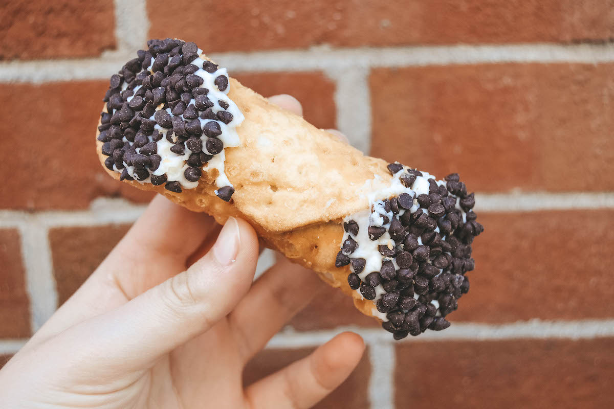 A cannoli being held in front of a brick wall