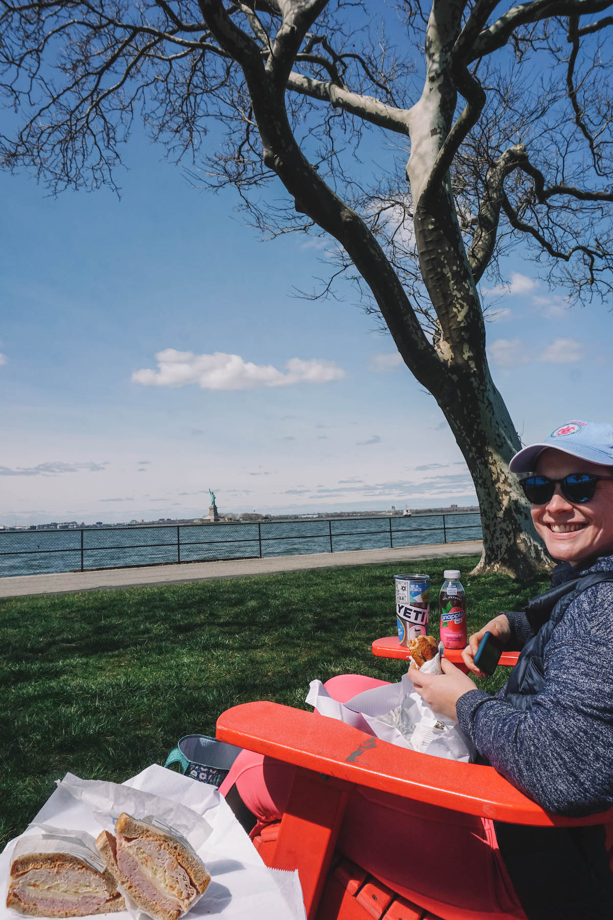 Woman smiling with lunch on Governors Island, with Statue of Liberty in the distance. 