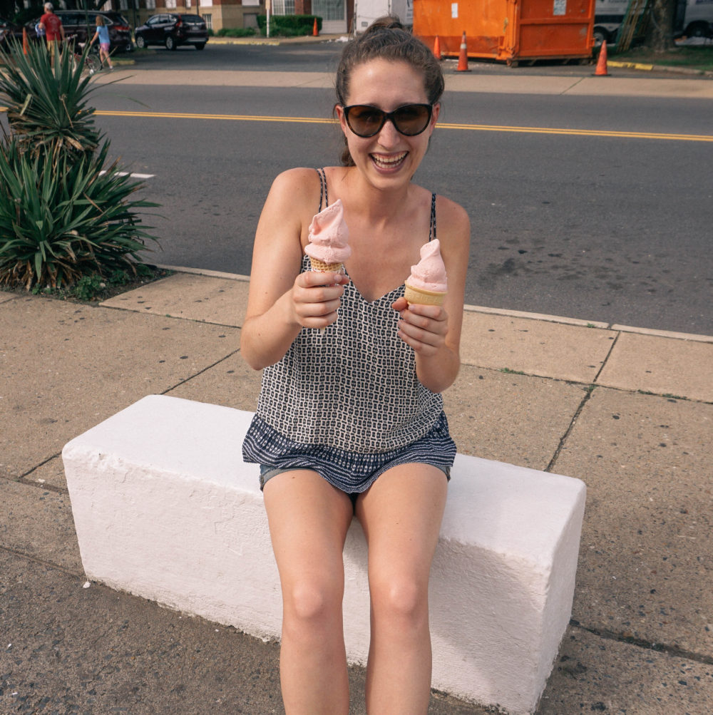 Woman holding up two ice cream cones and smiling. 