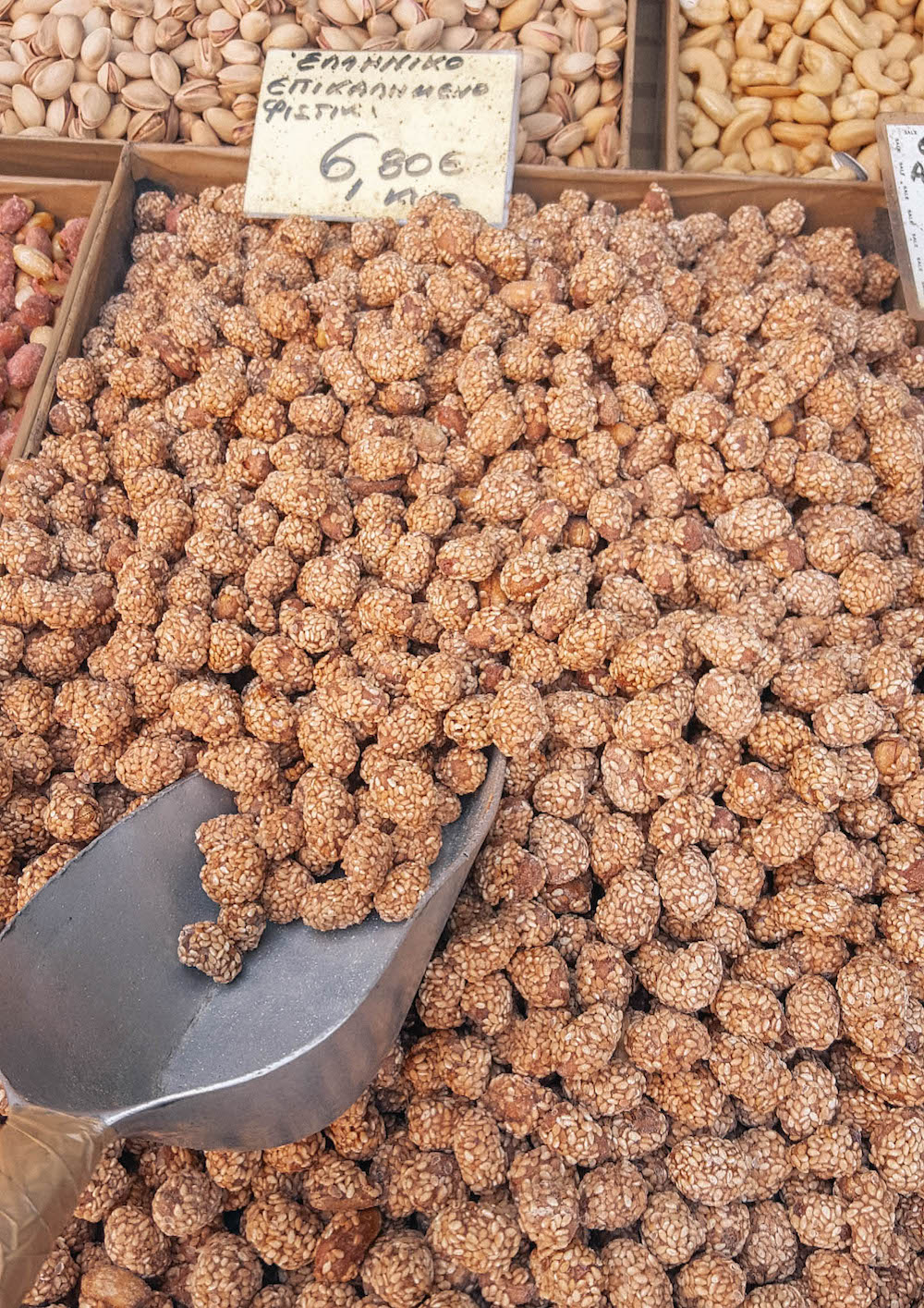 A bin of honey and sesame peanuts, with a metal scoop. 
