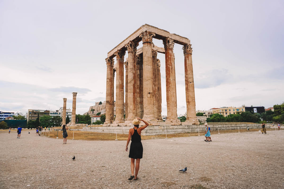 A woman walking towards Temple of Olympican Zeus in Athens on a cloudy day. 