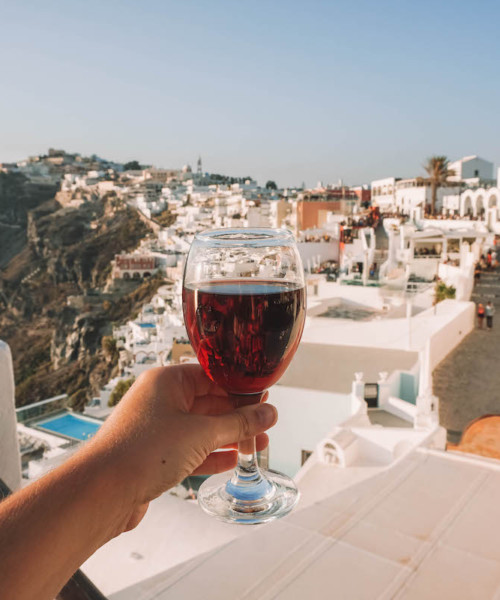 A glass of wine being held aloft in front of a Santorini sunset.