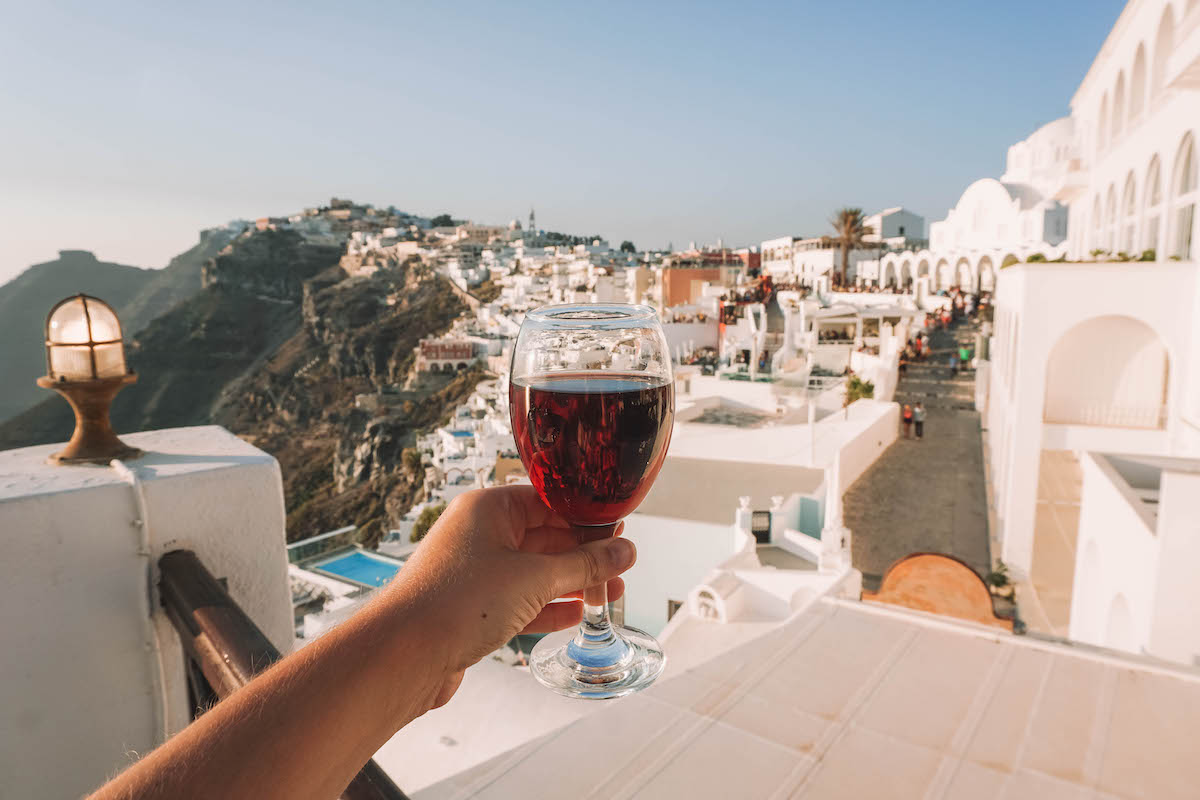 A glass of wine being held aloft in front of a Santorini sunset.