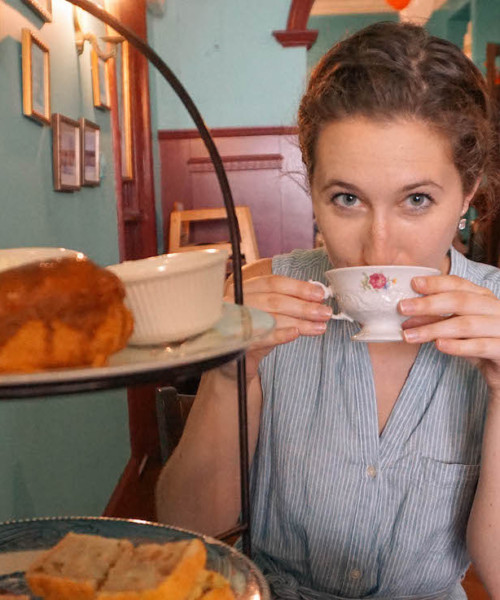 A woman holding a cup of tea to her mouth, inside Alice's Tea Cup in NYC.