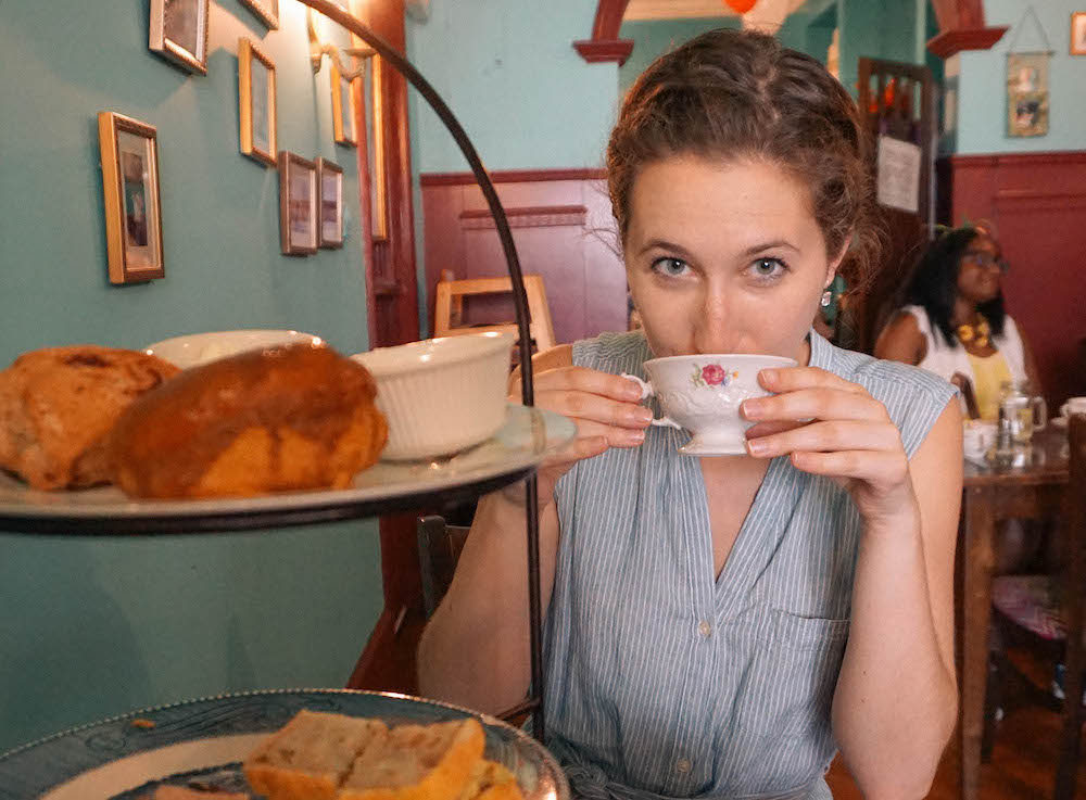 A woman holding a cup of tea to her mouth, inside Alice's Tea Cup in NYC. 