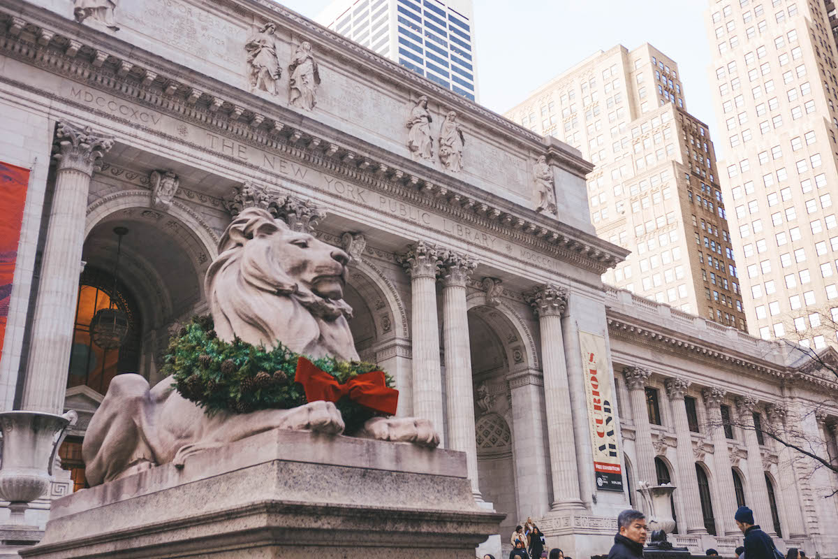 Stone lion in front of the NYPL building, decorated with a wreath. 