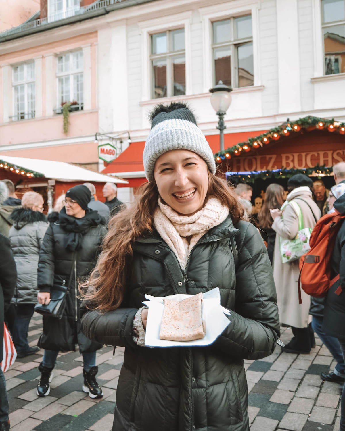 Woman holding crepe and smiling at a Christmas market.