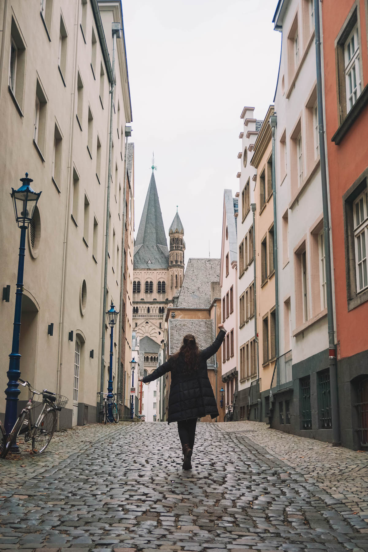 A woman holding arms aloft in a street in the Cologne Old Town