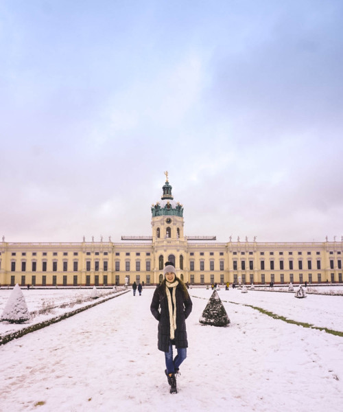 Woman standing in front of Charlottenburg Palace in Berlin. It's covered in snow.