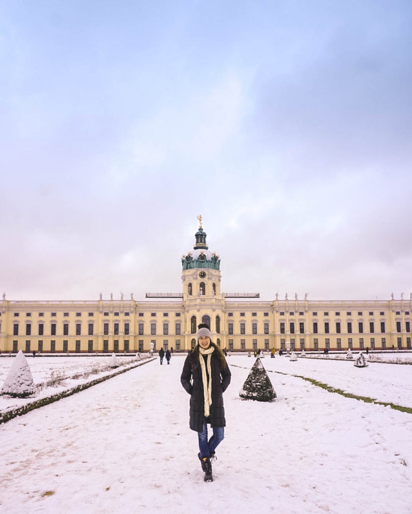 Woman standing in front of Charlottenburg Palace in Berlin. It's covered in snow.