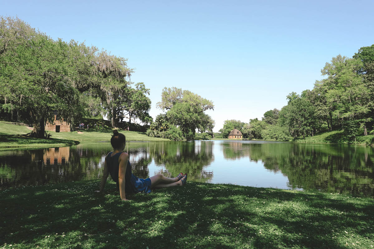 Woman leaning back on her hands, sitting by pond at Middleton Place. 