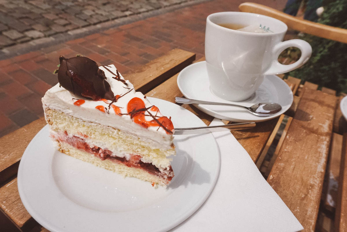 A cup of tea and a slice of strawberry cake on a white plate.
