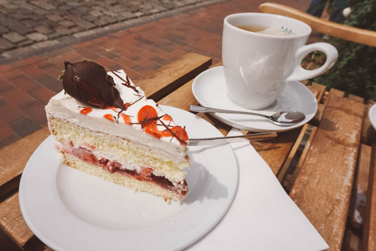 A cup of tea and a slice of strawberry cake on a white plate. 