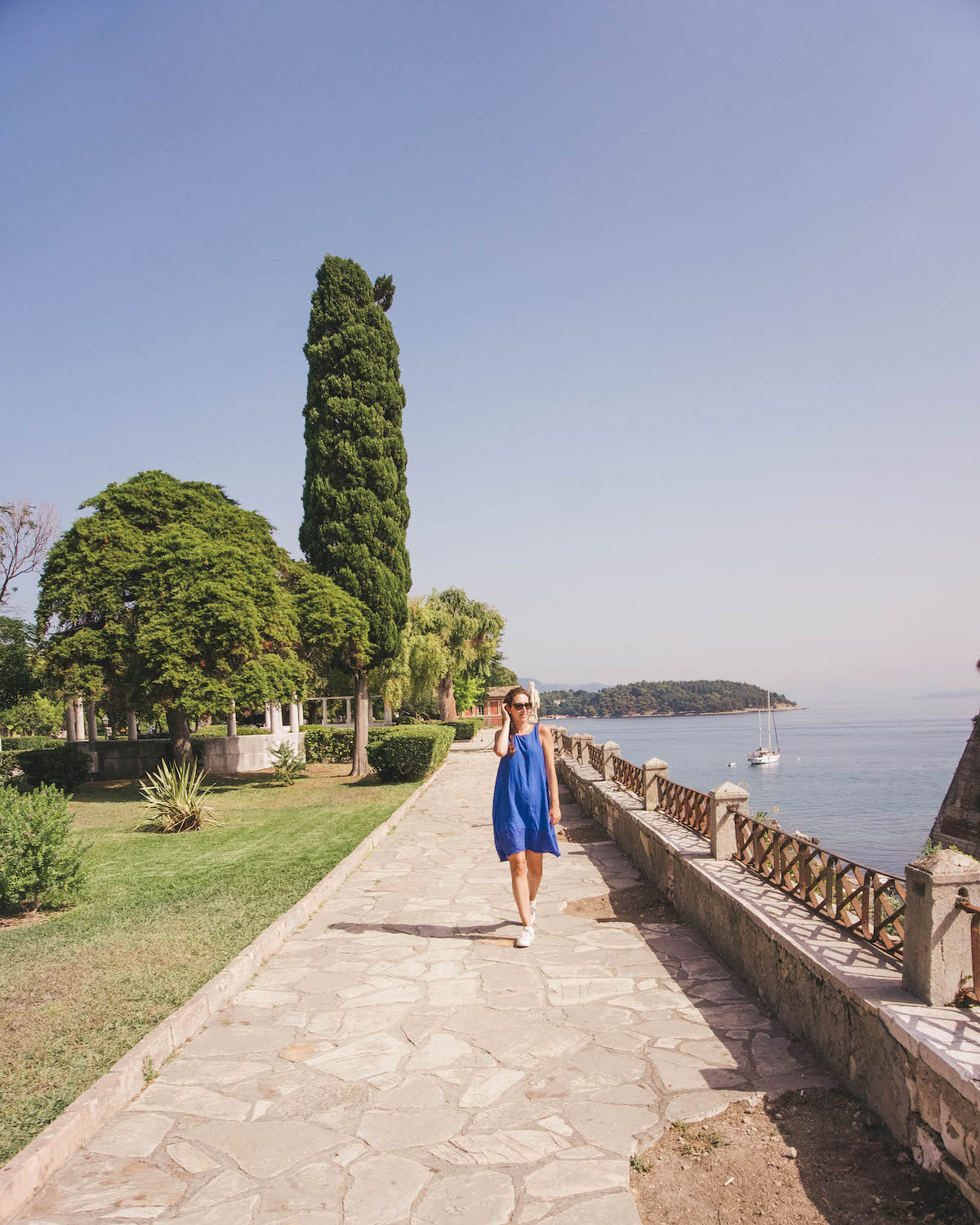 Woman in blue dress walking along gardens in Corfu. 