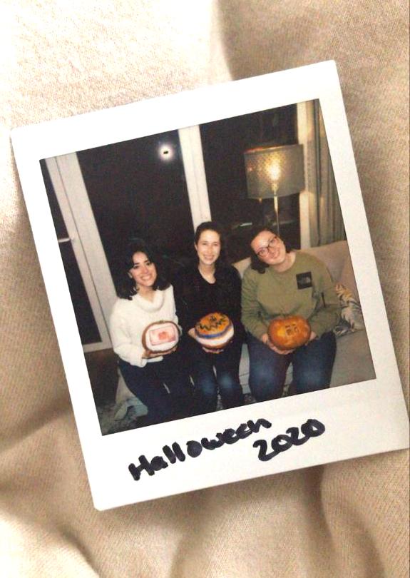 A polaroid photo showing three woman holding decorated pumpkins. 