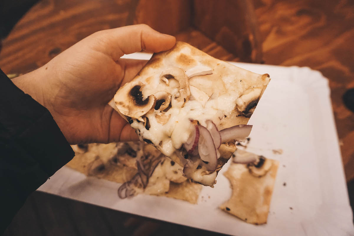 A slice of flammkuchen being held aloft