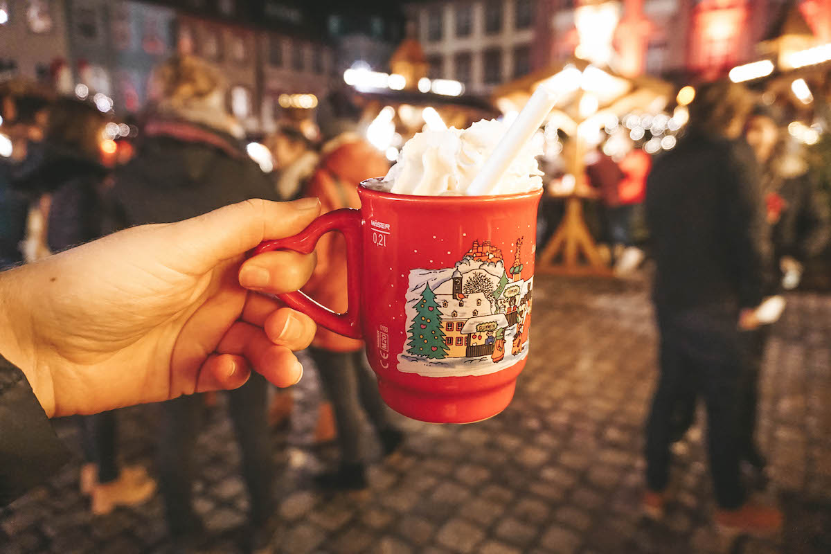 A mug of hot chocolate with whipped cream being held aloft