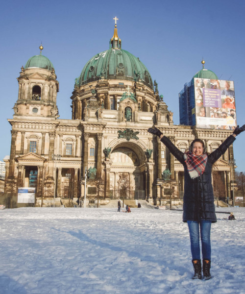 Woman smiling with hands raised in front of the Berliner Dom, in winter.