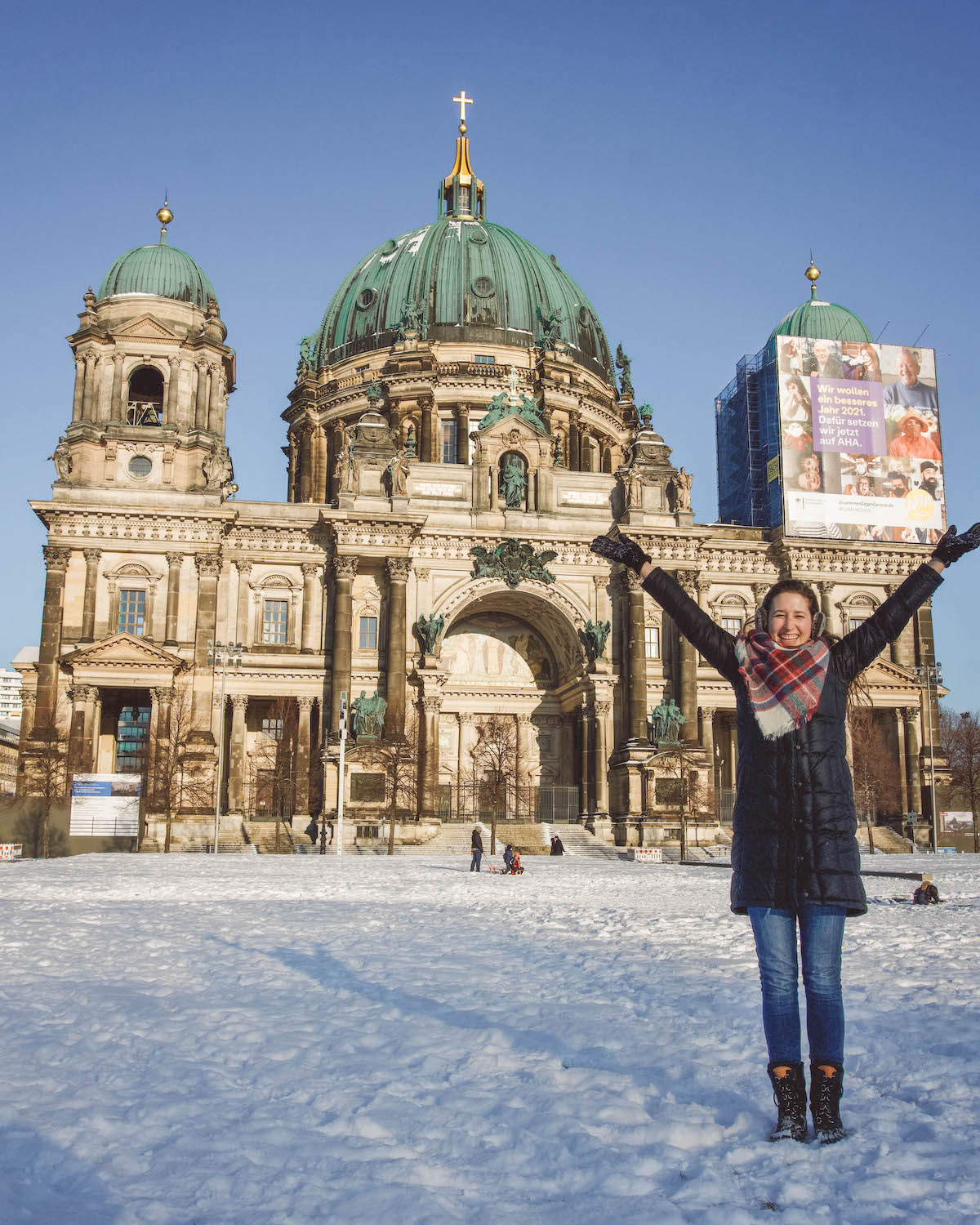 Woman smiling with hands raised in front of the Berliner Dom, in winter. 