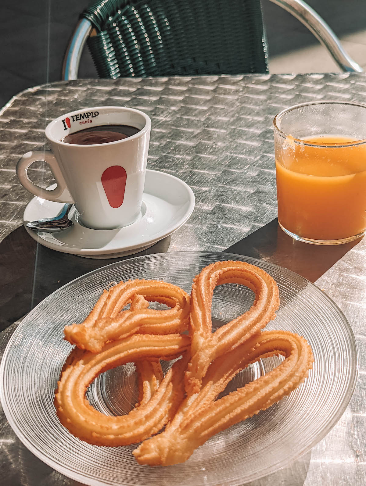 Churros, orange juice, and Spanish hot chocolate on a metal table top.
