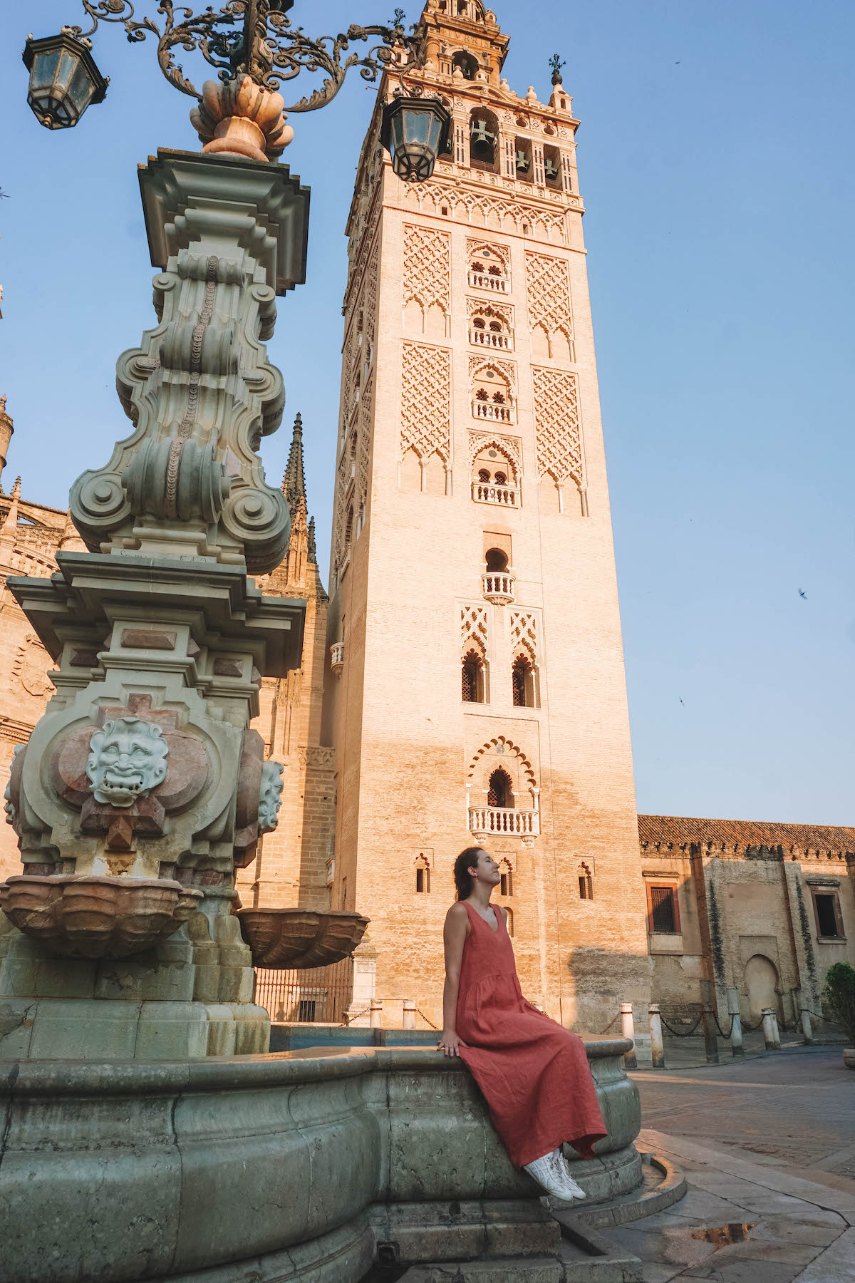 Woman sitting on fountain in front of Seville's La Giralda.
