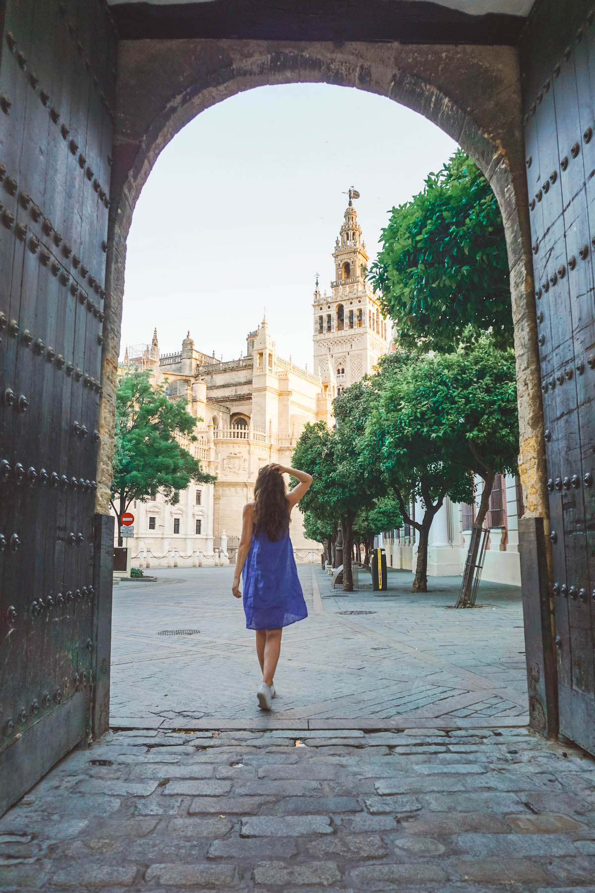 A woman in a blue dress walking through an archway in Seville, Spain. La Giralda is in the background. 