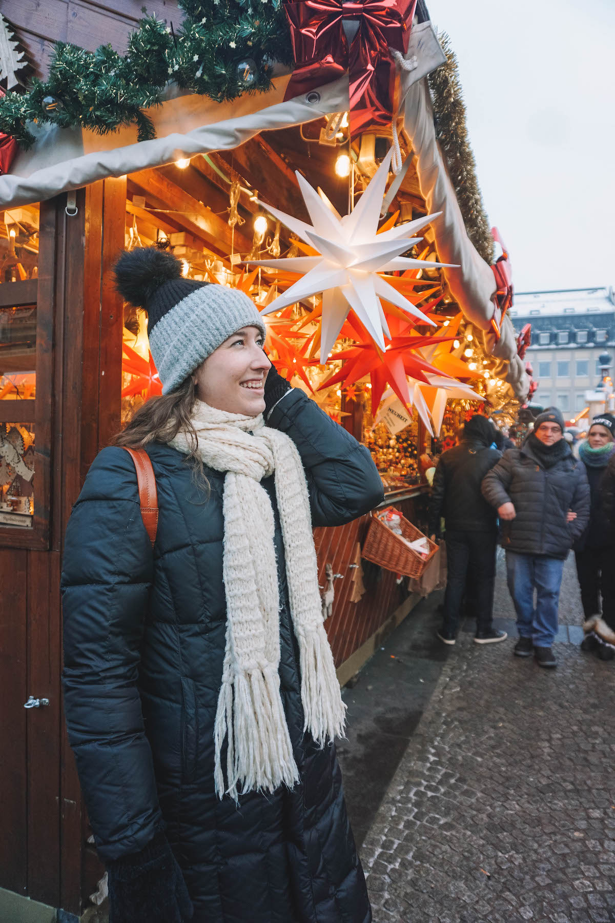 A woman smiling in front of paper stars at a German Christmas market