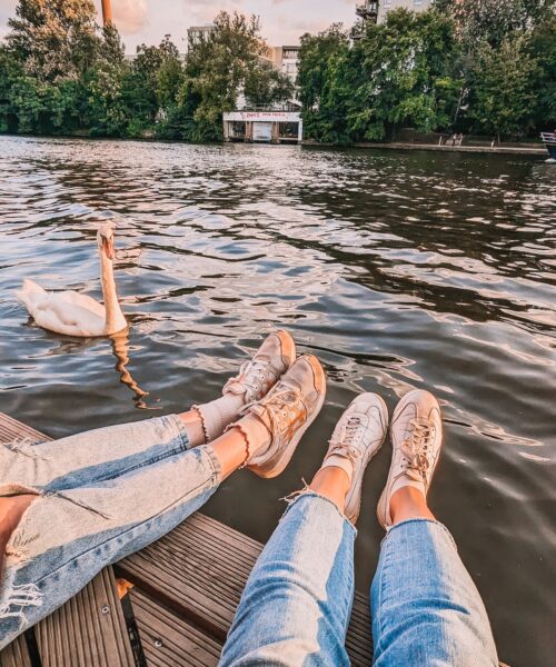 Two pairs of feet dangling over the Spree River, with a swan