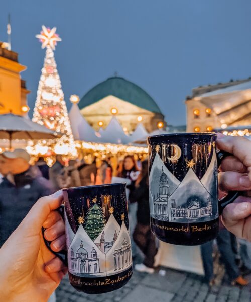 Two mugs of mulled wine being held aloft at Berlin Christmas market