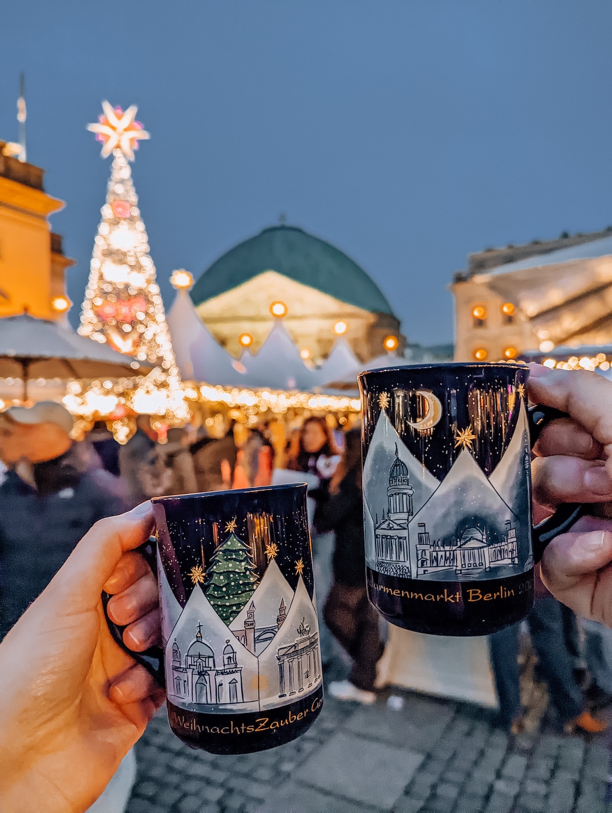 Two mugs of mulled wine being held aloft at Berlin Christmas market